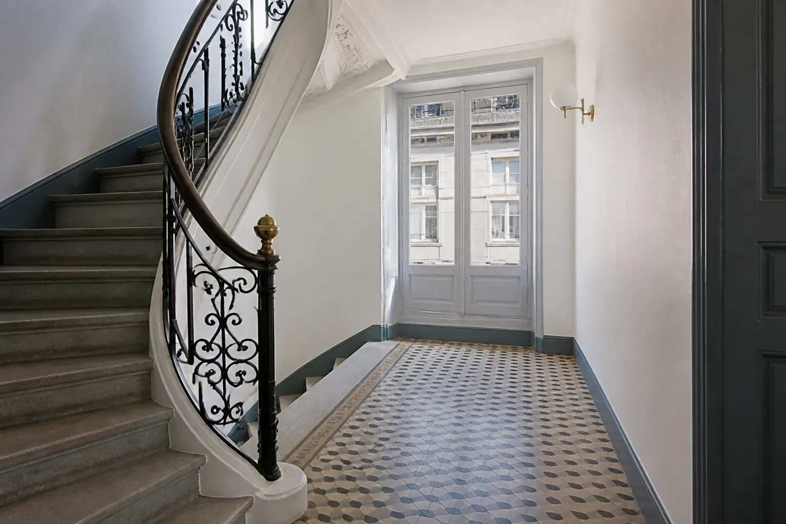 Cage d’escalier d’immeuble ancien rénovée, rampe en fer forgé repeinte et carrelage de palier à motifs nettoyé