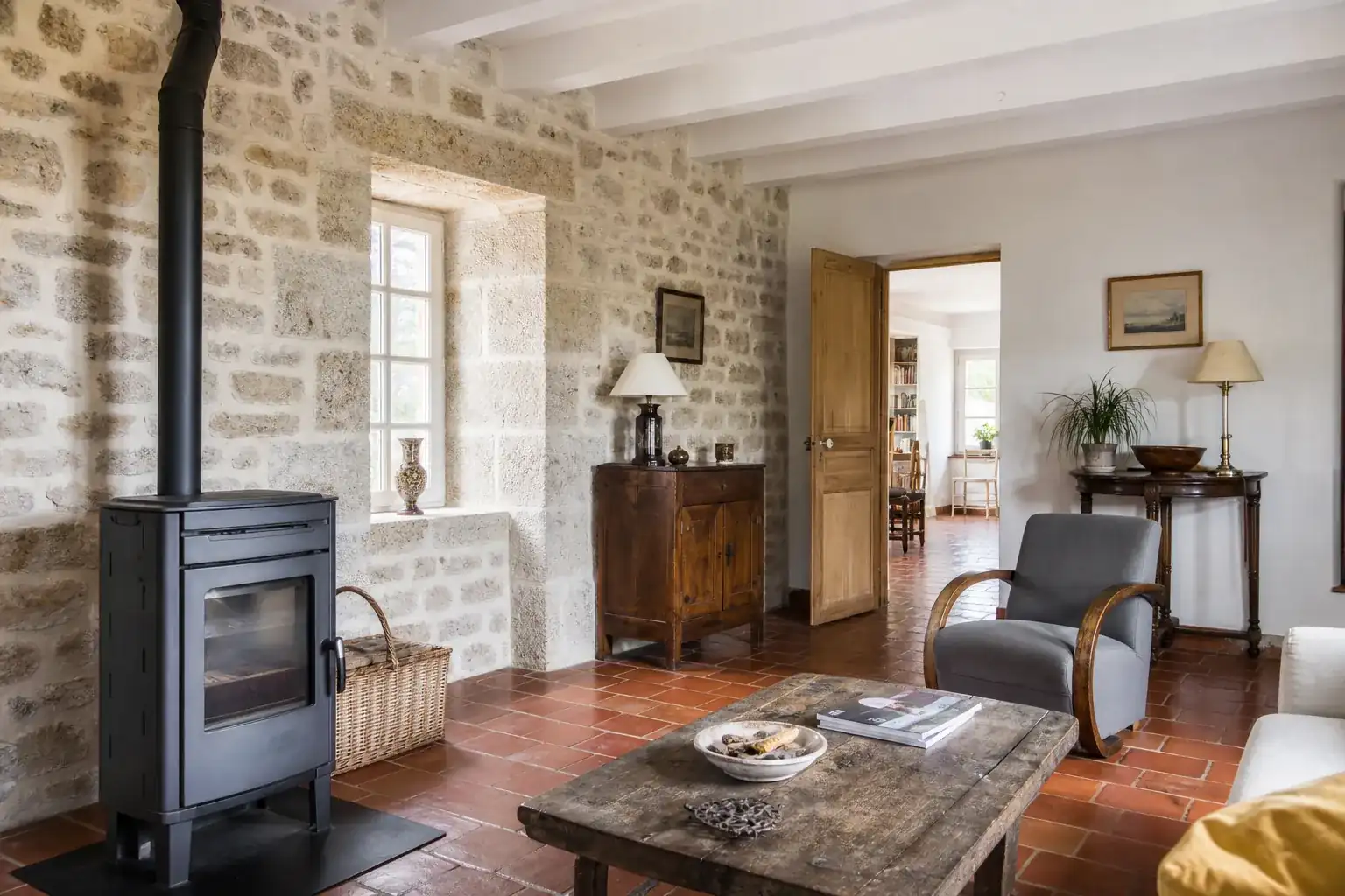 Pièce rénovée d’une maison de coteau, mur de moellons rejointoyé à la chaux, tomettes anciennes et poêle à bois