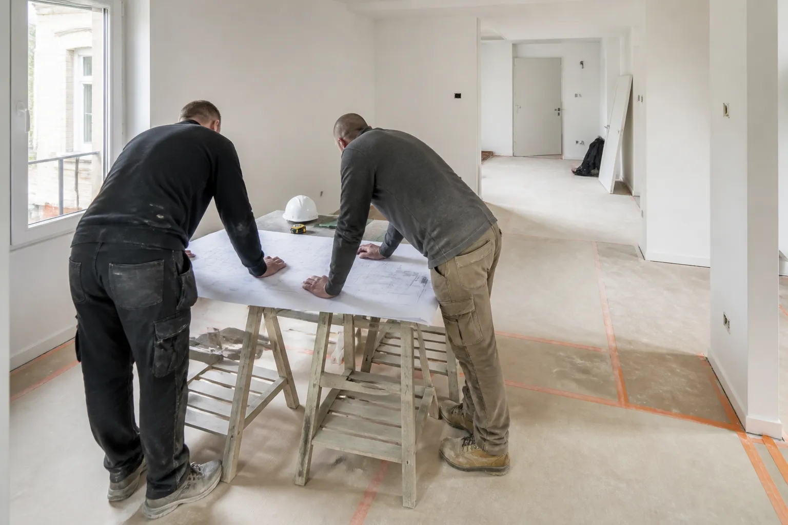 Deux artisans penchés sur des plans déroulés sur des tréteaux dans un appartement en travaux